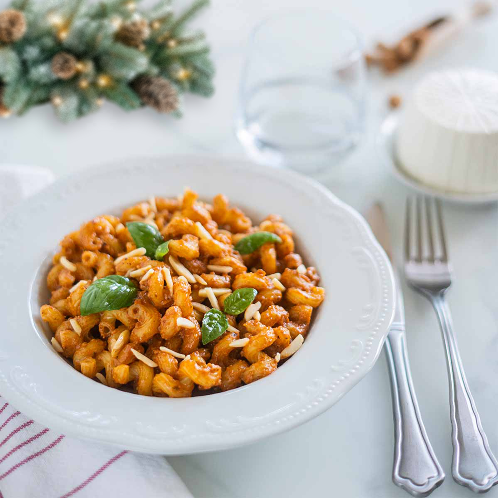 Piatto di cellentani con pesto siciliano e mandorle tostate con una ghirlanda natalizia sullo sfondo