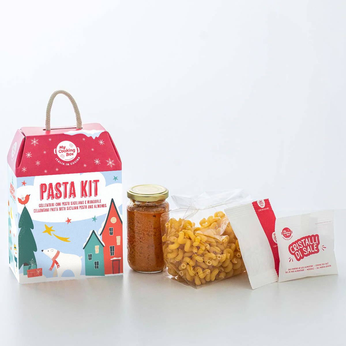 Confezione graficata natalizia con accanto sugo, pasta, sale e mandorle per realizzare la ricetta